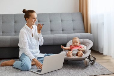 Beyaz gömlek ve kot pantolon giyen, beyaz saçlı, beyaz saçlı, bebekle sallanan sandalyesinde vakit geçiren beyaz bir kadının yatay görüntüsü..