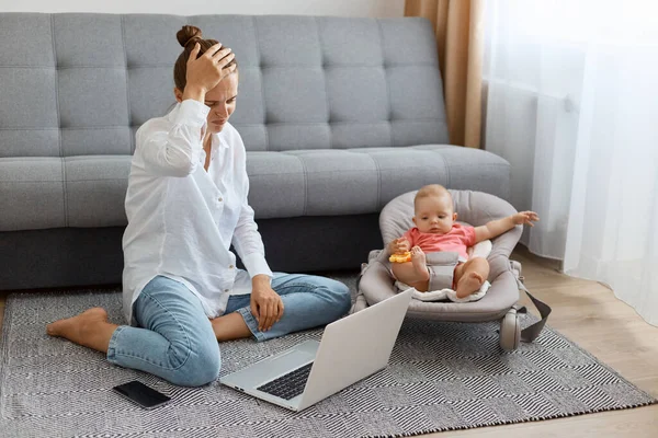 Beyaz gömlek ve kot pantolon giyen üzgün bir kadın. Annesi yerde kızıyla oturuyor ve dizüstü bilgisayarda çalışıyor. Sorunları var..