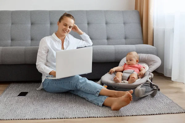 Gevşemiş, iyimser bir kadın. Bun saç stili, beyaz gömlek ve kot giyen, kızının yanında poz veren, elinde not defteri olan, ekrana bakan, film izleyen..