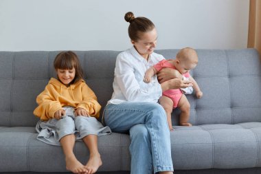 Çocuklarıyla birlikte kanepede oturan ve oynayan yetişkin bir annenin portresi. Doğum iznini küçük tatlı çocuklarıyla geçiren bir kadın. Büyük beden giyinen büyük bir kız..