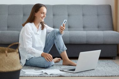 Beyaz gömlekli, kot pantolonlu, elinde cep telefonu, elinde büyüleyici bir gülümseme, çalışan bir defterle telefona bakan mutlu bir kadının kapalı çekimleri..