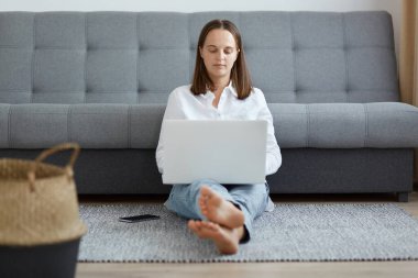 Beyaz gömlek ve kot pantolon giyen koyu renk saçlı beyaz bir kadının tam boy portresi. İnternette çalışan kadın serbest yazar, yoğun pozitiflik ifadesiyle ekrana bakıyor..