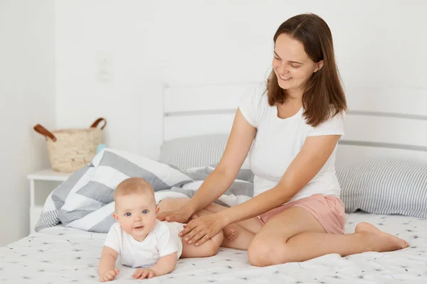Beyaz Tişörtlü Kısa Boylu Gülümseyen Bir Kadının Bebeğiyle Yatakta Oturduğu — Stok fotoğraf