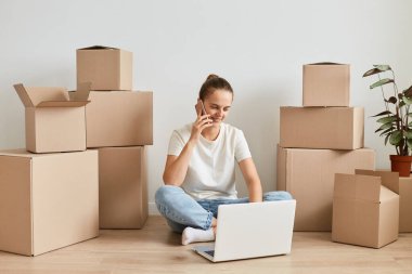 Beyaz tişörtlü, gülümseyen mutlu bir kadının tam boy portresi. Etrafı karton kutularla çevrili, dizüstü bilgisayarda çalışıyor, telefonda konuşuyor, defterde daktilo yazıyor..