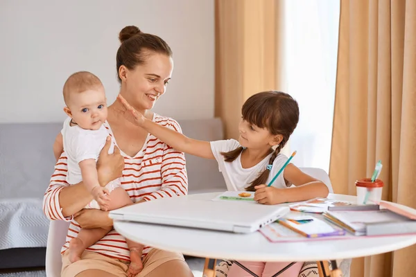 Portrait Smiling Young Mother Sitting Schoolgirl Infant Daughters Table Helping — Stock Photo, Image