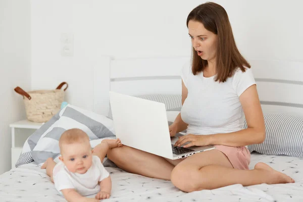 Astonished Dark Haired Woman Sitting Bed Her Infant Daughter Working — Stock Photo, Image