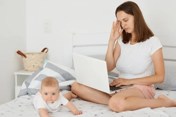 Portrait Tired Woman Sitting Bed Her Infant Daughter Working Online — Stock Photo, Image