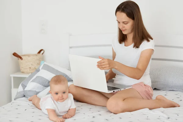 Indoor Shot Atractiva Mujer Concentrada Sentada Cama Con Hija Lactante —  Fotos de Stock