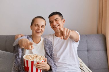 Çekici genç bir çiftin kanepede patlamış mısır ve uzaktan kumandayla oturup ilginç bir dizi ya da film izlediği, gülümseyip kamerayı işaret ettiği görüntüsü..