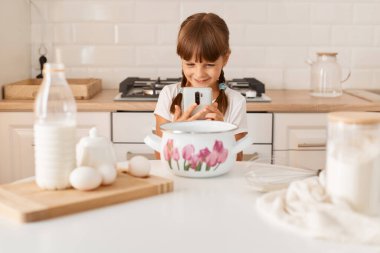 Gülümseyen sevimli küçük kız fırıncının portresi. Mutfakta pişirme malzemeleriyle birlikte. Ev yapımı hamur işi yaparken fotoğraf ya da video yapmak..
