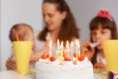 Mutlu anne ve çocukların bulanık arka planda olduğu mumlu doğum günü pastası portresi..