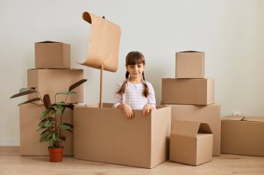 Saçı örgülü, el yapımı, karton kutudan yelkenliyle oynayan, karton paketlerle çevrili mutlu, koyu renk saçlı küçük kızın portresi, başka bir eve taşınıyor..