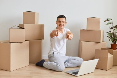 Kapalı alanda çalışırken kameraya bakıp bakan, sıradan kıyafetler giyen, sıradan giyinen esmer adamın resmi. Emlak acentesini seçmenizi istiyorum..