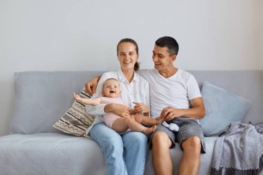 Tatmin olmuş kadın ve erkek portresi, kanepede oturup pozitif duygu ve mutluluğu ifade etmek, çocuklu çift, gülümseyerek kameraya bakmak..