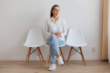 Beyaz gömlek ve kot pantolon giyen hasta bir kadının portresi. Doktor kuyruğunda oturuyor. Karın ağrısı çeken bir kadın..