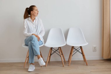 Beyaz gömlek ve kot pantolon giymiş, kuyrukta oturan ve ağzı açık bir şekilde başka tarafa bakan genç bir kadının kapalı çekimleri, hayret verici bir şey görür..