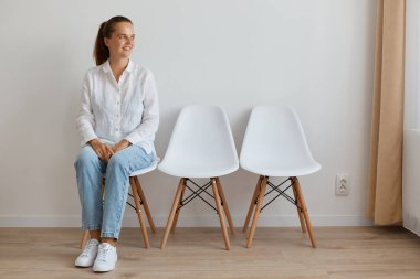 Beyaz gömlek ve kot pantolon giyen çekici, koyu renk saçlı bir kadının kuyrukta oturduğu ve bakışlarını kaçırdığı, birini beklediği, iş görüşmesi yaptığı görüntüsü..