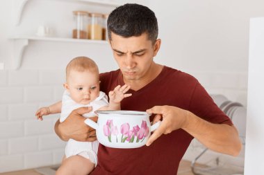Esmer, beyaz tenli, kestane rengi bir tişört giyen, elinde bebek kızıyla mutfakta duran, tencerede çorba kokan, berbat kokan, taze yemek pişirmesi gereken bir adam görüntüsü..
