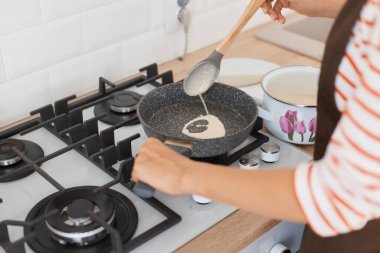 Kızartma tavasında el kızartmalı krep portresi, elinde kaşık, ailesine kahvaltı hazırlayan, çizgili tüylü ve önlüklü kimliği belirsiz bir kadın..