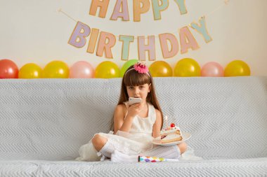 Koyu renk saçlı, pembe saçlı, kanepede oturan, beyaz şık elbiseli, elinde doğum günü pastası ve cep telefonu olan, sesli mesaj kaydeden, davetlileri davet eden küçük bir kız resmi..