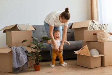 Küçük kızıyla oynayan, ilk adımlarını atmasına yardım eden, ağlayan bebeğini sakinleştirmeye çalışan, eşyalarını yerleştiren ve yerleştiren genç bir annenin tam boy portresi..