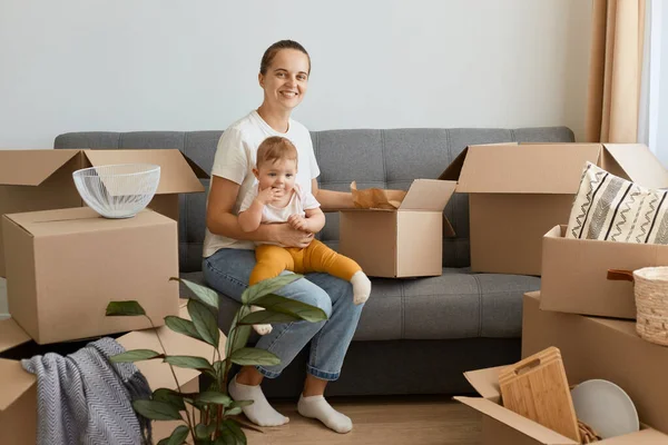 Beyaz tişörtlü beyaz kadın portresi kanepeye oturmuş elinde bebek bebekle kutusunu açıyor, yerini değiştiriyor, büyüleyici bir gülümsemeyle kameraya bakıyor..