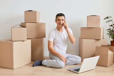 Beyaz adamın evden çıkmadan önce yerde dizüstü bilgisayarla otururken çekilmiş bir fotoğrafı. Karton kutuların arasında cep telefonuyla konuşan, teslimat siparişi veren, kameraya bakan biri..