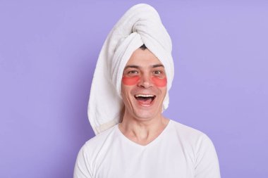 Gözlerinin altında yamalar olan beyaz bir adamın görüntüsü havluya sarılmış, heyecanlı bir yüz ifadesiyle kameraya bakıyor, evde sabah ameliyatları yapıyor, mutlu hissediyor..