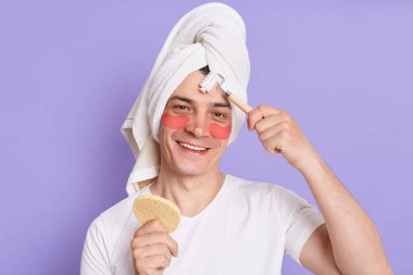 Sabahları gülümseyen yakışıklı adamın kozmetik ameliyatlar yaparken, göz altında yamalarla dikilirken ve yuvarlaklarla masaj yaparken, neşeli bir ifadeyle kameraya bakarken,.