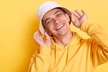 Kapalı mekanda, sarı arka planda izole edilmiş bir şekilde poz veren ve mutluluğu ifade eden hoş ve çekici bir adamın fotoğrafı..