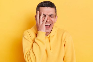 Kafkasyalı üzgün bir adamın portresi sıradan bir kapüşonlu giyiyordu, ağlıyordu, kötü haberler dinliyordu, yüzünün yarısını palmiye ile kaplıyordu, sarı arka planda izole bir şekilde poz veriyordu..