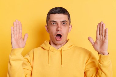 Sarı arka plan üzerinde izole edilmiş, büyük boy, reklam alanı gösteren, sıradan tarz kapüşonlu giyinen, şaşırmış bir adamın kapalı mekândaki fotoğrafı..