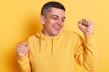 Zevkten dört köşe olmuş yakışıklı bir adamın portresi sarı arka planda izole edilmiş bir şekilde poz veriyor. Kazanan jestini yumruklarıyla, çığlıklarıyla, zaferini kutluyor..