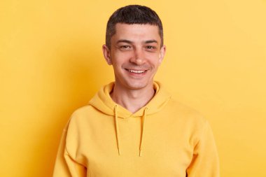 Mutlu bir yüz ifadesiyle, mutlu bir ruh hali içinde, sarı arka planda izole edilmiş rahat bir şekilde poz veren mutlu bir adamın yatay görüntüsü..