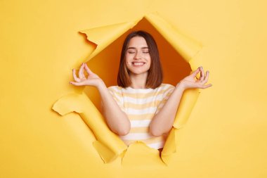 Kafkasyalı sakin bir kadının portresi yırtık bir kağıt deliğinde duruyor, sakinleşmek için yoga yapıyor, meditasyon yapıyor, sarı arka plandaki buluşları inceliyor..