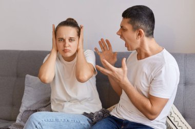 Genç bir kadın ve erkeğin tartışması, kanepeye oturup çığlık atması, kocanın çığlık atması, kadınların gözlerini kapatması, sorunların olması, ailenin beyaz t-shirt giymesi..