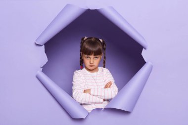 Saçları örgülü, mor arka planda çığır açan, elleri bağlı, kederini ifade eden üzgün küçük bir kızın yatay görüntüsü..