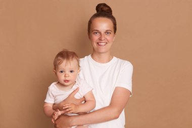 Tatmin olmuş bir anne kucağında küçük bir kız bebeği, mutlu bir aile birlikte eğleniyor, annesinin kollarında sevimli bir çocuk, kahverengi arka planda izole edilmiş anne ve çocuk..