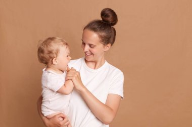 Annenin küçük kızla oynadığı, mutlu bir ailenin evde eğlendiği, annesinin kollarında neşeli tatlı bir çocuğun kahverengi arka planda izole edilmiş anne ve çocuğunun olduğu bir fotoğraf..