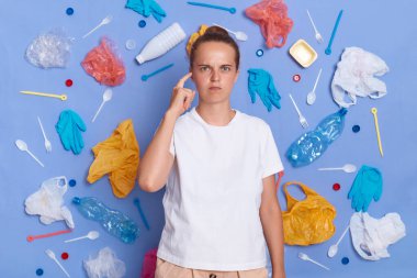 Ekoloji sorunu ve çevre kirliliği. Ciddi üzgün bir kadın kafasını işaret ediyor, gezegeni nasıl kurtaracağını düşünüyor, plastik atıkları tekrar kullanıyor, kirliliği durduruyor..