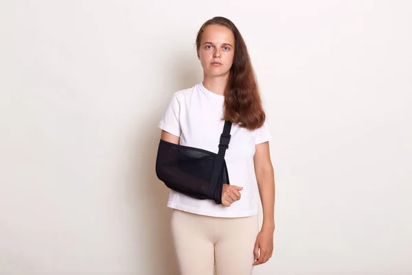 Portrait of sick arm broken Caucasian woman with arm sling supported on her hand, being injured by accident and healthcare, posing isolated on white background.