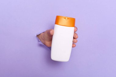 Mor duvar deliğinde kozmetik şişesi ya da şampuanı tutan kişinin eline yakın çekim, tasarımınız için kopya alanı, tanıtım metni için reklam arası. Bayrak satışları.