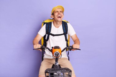 Scooter 'da yemek dağıtan, gülen, keyfi yerinde mor arka planda izole bir şekilde poz veren komik mutlu teslimatçının yatay çekimi..