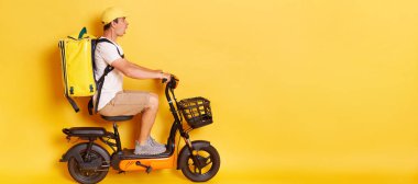 Beyaz tişörtlü, şapkalı, motosiklet süren, kazadan korkan, korkmuş ve şok olmuş, sarı arka planda izole edilmiş bir teslimatçı portresi..