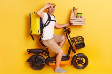 Kapalı mekanda, sürpriz erkek kuryenin sıradan kıyafetler giyip sırt çantasıyla pizza dağıtırken ve müşteriye kahve dağıtırken, şaşırmış bir yüz ifadesiyle uzaklara bakarken..