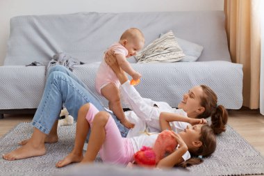 Side view full length portrait of smiling woman holding baby daughter in hands while lying on floor, mother playing with her children, enjoying to spend time together.