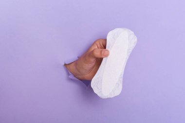 Photo of female hand holding daily sanitary pad through torn purple paper background, women health care during period, gynecology.