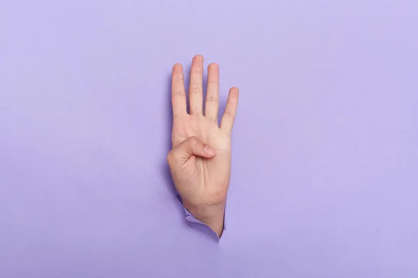 Person Hand Sticks Out Hole Paper Lilac Background Four Fingers — Foto de Stock