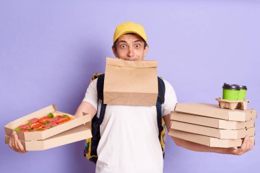 Sarı şapkalı, tişörtlü, elinde pizza, paket kahve ve kağıt paketiyle menekşe arka planda yalnız poz veren servis elemanının kapalı çekimleri var..