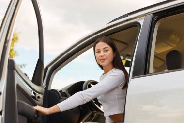 Uzun siyah saçlı, beyaz gömlekli güzel bir kadının portresi. Arabanın kapısını açıyor ve kameraya bakıyor. Arabasından iniyor..